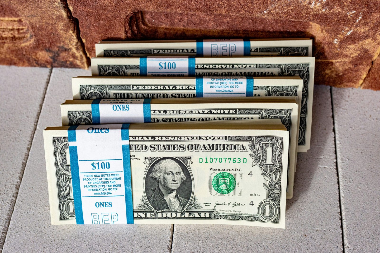 three stacks of one hundred dollar bills on a tile floor