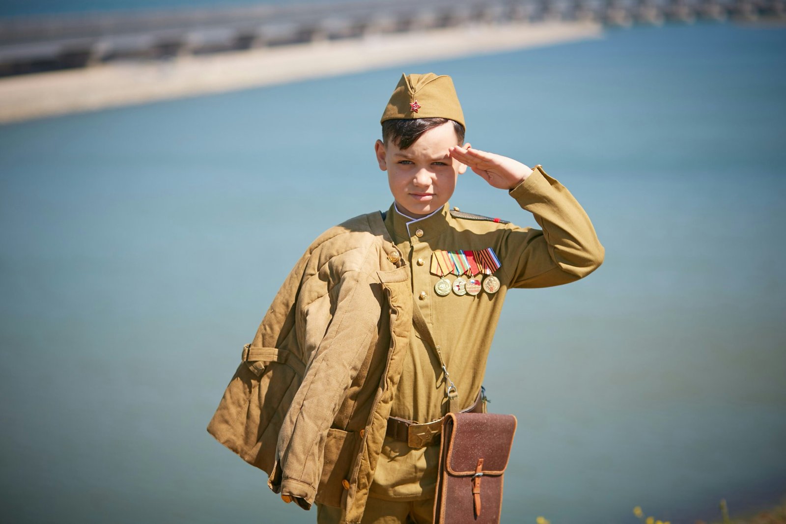 a boy in a uniform saluting in front of a body of water