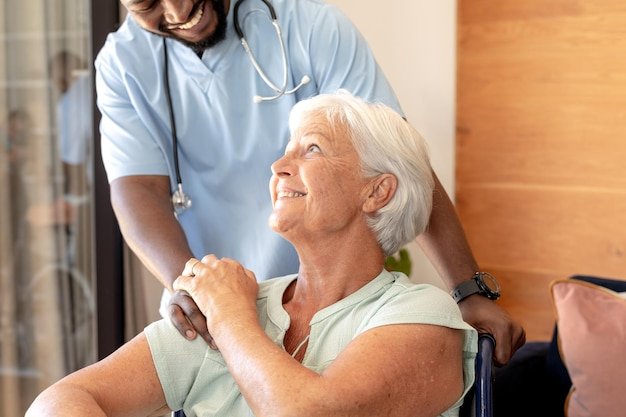 African american male health worker supporting caucasian senior woman sitting on the wheelchair