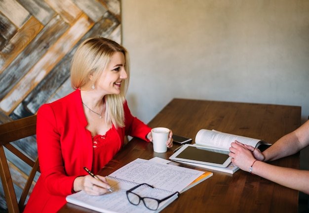 Attractive young woman in a red jacket works at a table with papers and devices