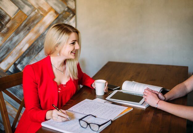 Attractive young woman in a red jacket works at a table with papers and devices