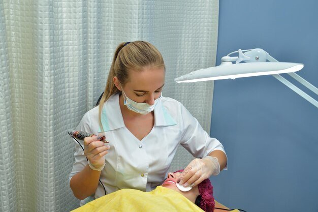 In a beauty salon a cosmetologist makes permanent lip makeup for a European girl