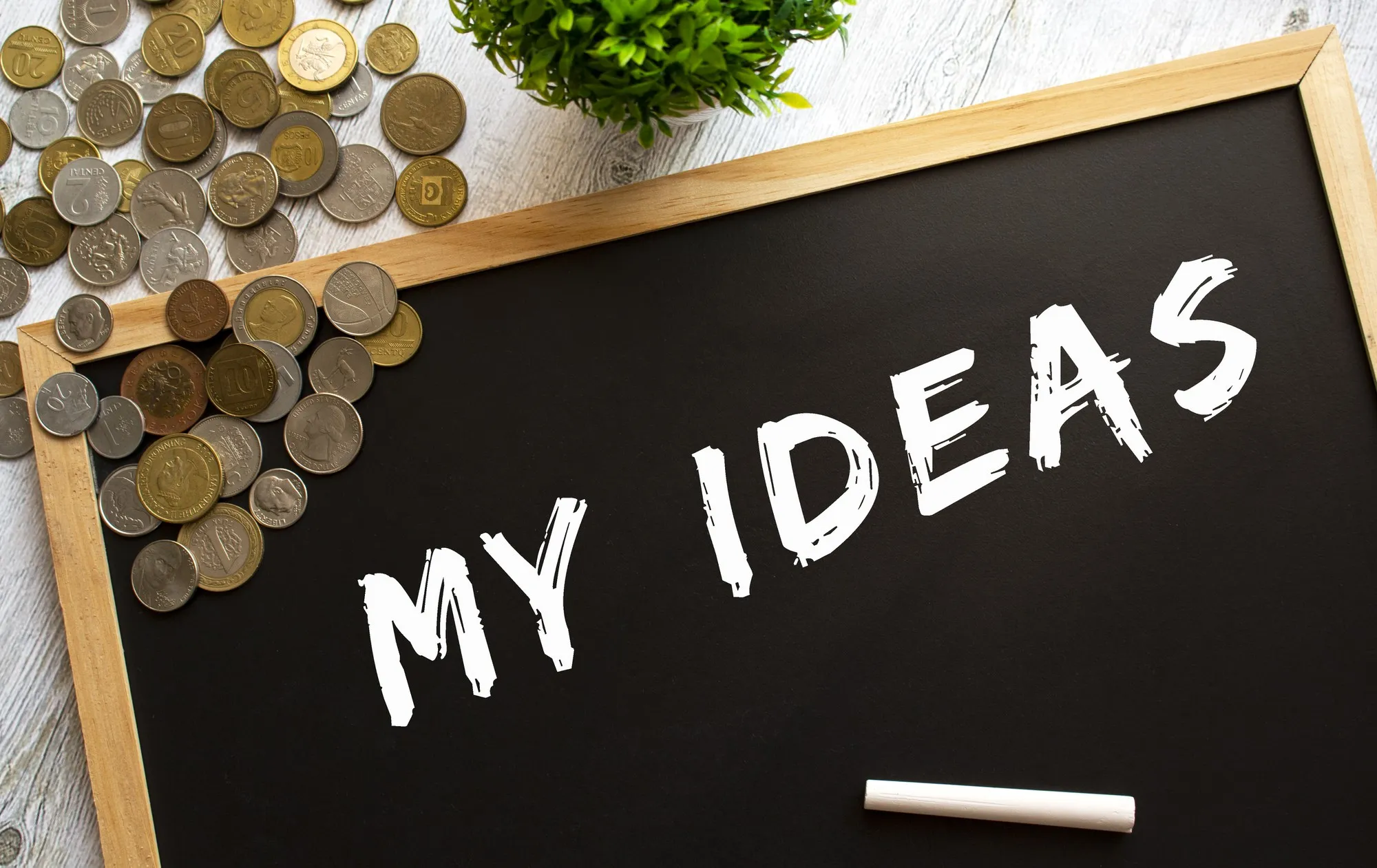 Blackboard with the text MY IDEAS and metal coins on a gray wooden table. Financial concept.