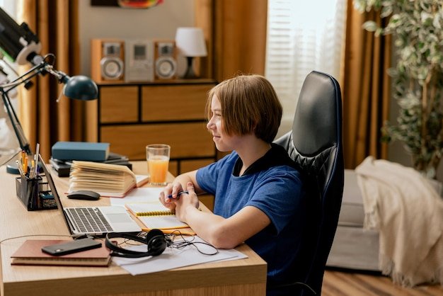 Boy with longer hair sits at desk in office drinks orange juice does homework studies takes notes wa