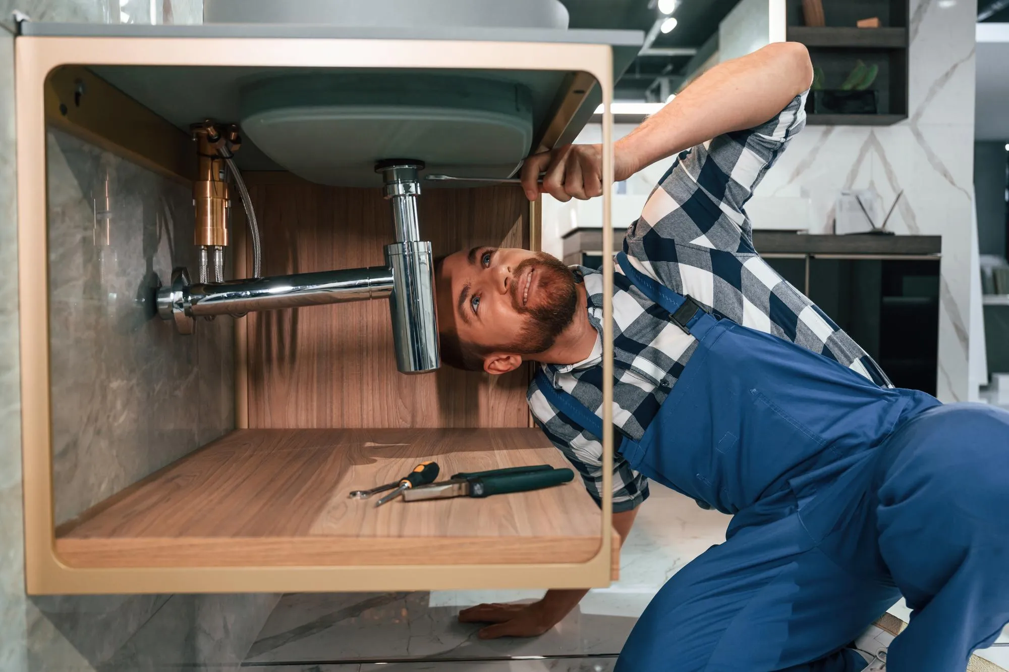 Busy by repairing siphon Plumber in blue uniform is at work in the bathroom