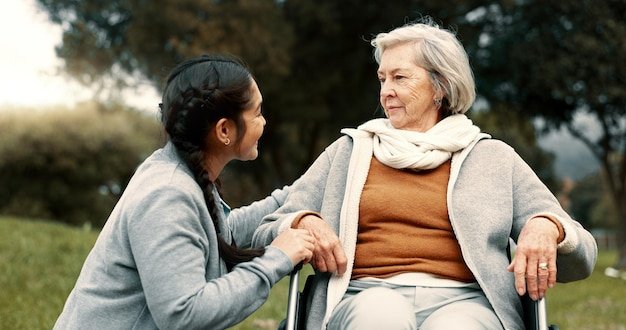 Caregiver helping woman with disability in park for support trust and care in retirement Nurse talking to happy senior patient in wheelchair for rehabilitation therapy and conversation in garden