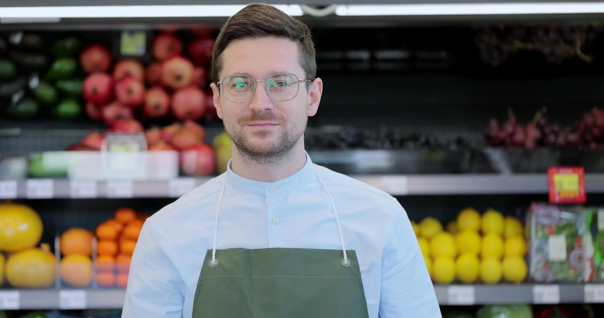Close up portrait of happy man worker in glasses wearing apron standing in supermarket and looking at camera Retail business