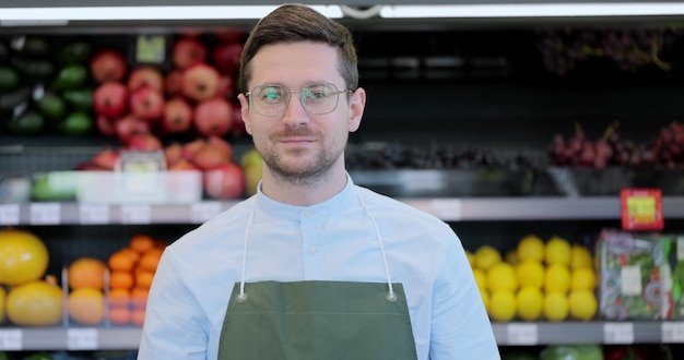 Close up portrait of happy man worker in glasses wearing apron standing in supermarket and looking at camera Retail business