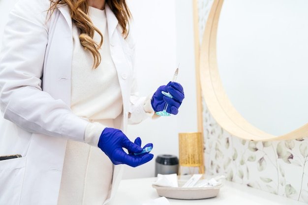 Closeup of unrecognizable medic in white coat and blue gloves readying a syringe with hyaluronic acid for aesthetic treatment