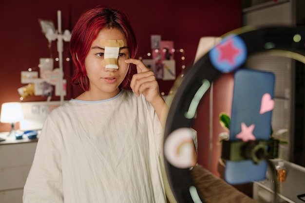 Cute girl with bandage on her nose touching under eye area