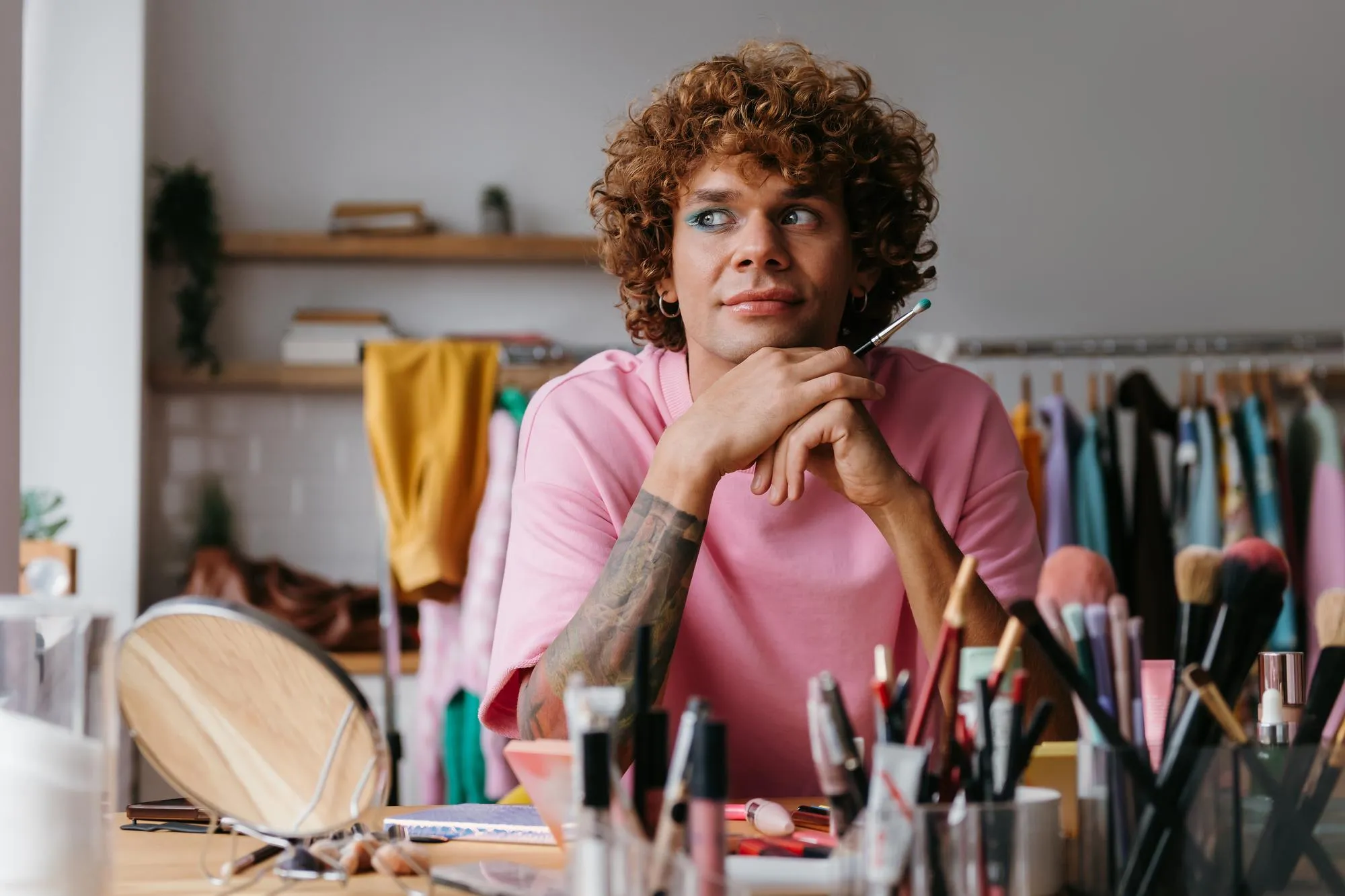 Dreamful young gay man looking away while applying makeup at home