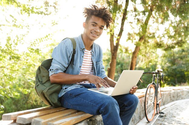 Emotional young guy in park outdoors using laptop
