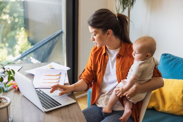 Female entrepreneur working on laptop while babysitting her daughter at home.