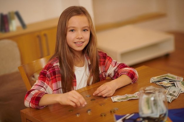 Financial literacy. A long-haired girl in a plaid shirt counting her savings