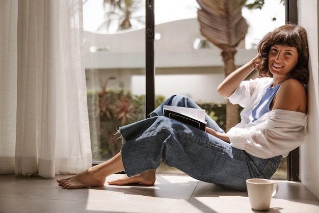 Full view brunette hair woman reading book smiling at camera