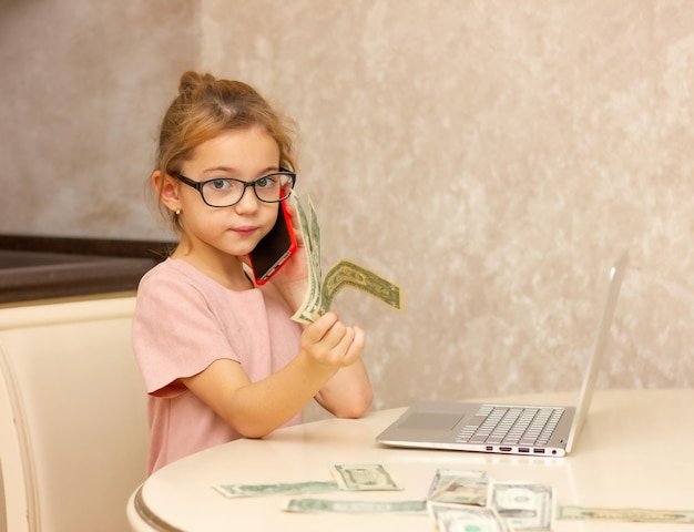 Girl in glasses with dollar bills and a computer plays accountant the concept of remote work in qu