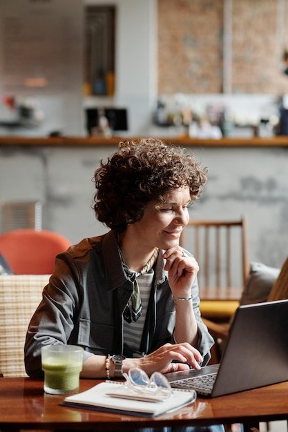 Happy middle aged businesswoman or freelancer networking by table in cafe