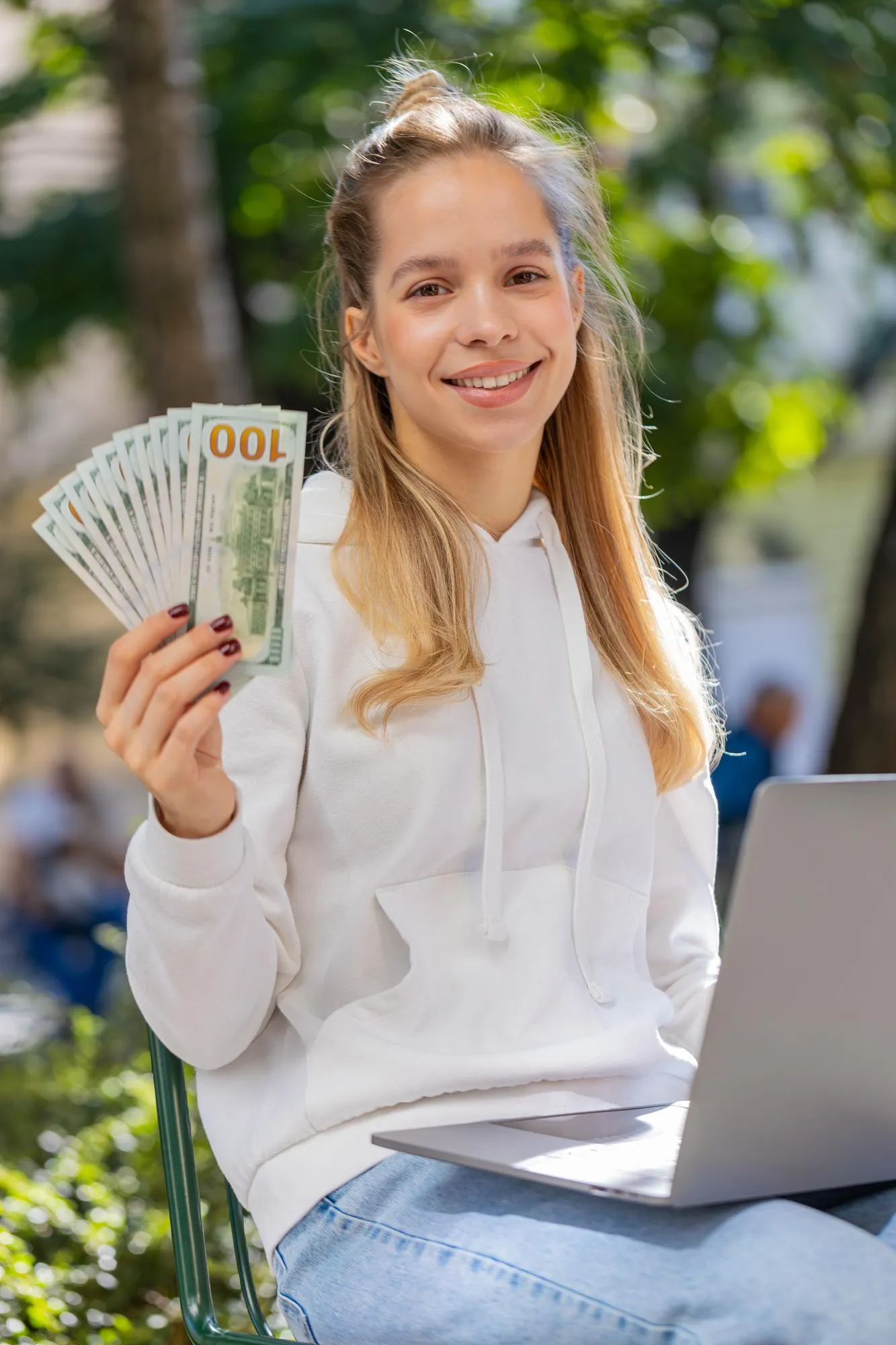 Happy rich woman using laptop winner victory holding cash money in dollar banknotes sitting on chair