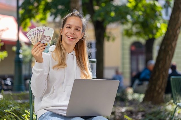 Happy rich woman using laptop winner victory holding cash money in ukrainian hryvnias uah banknotes
