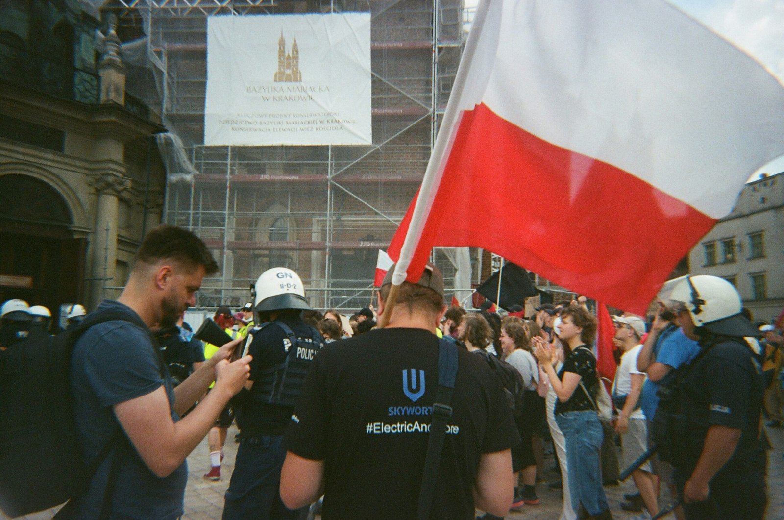 Crowd with polish flag near scaffolding and police.