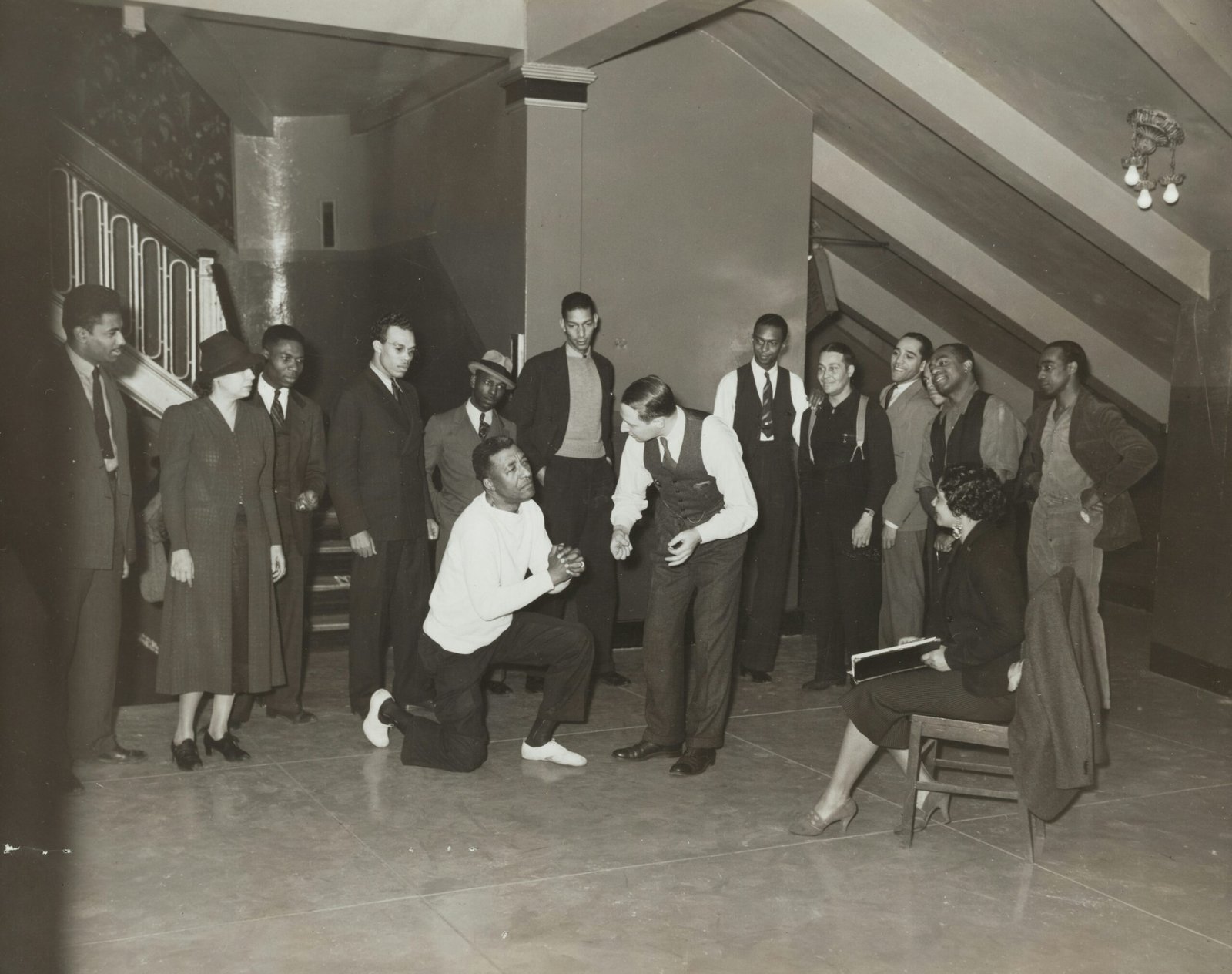woman sitting and facing man taking a knee beside standing men and women indoors