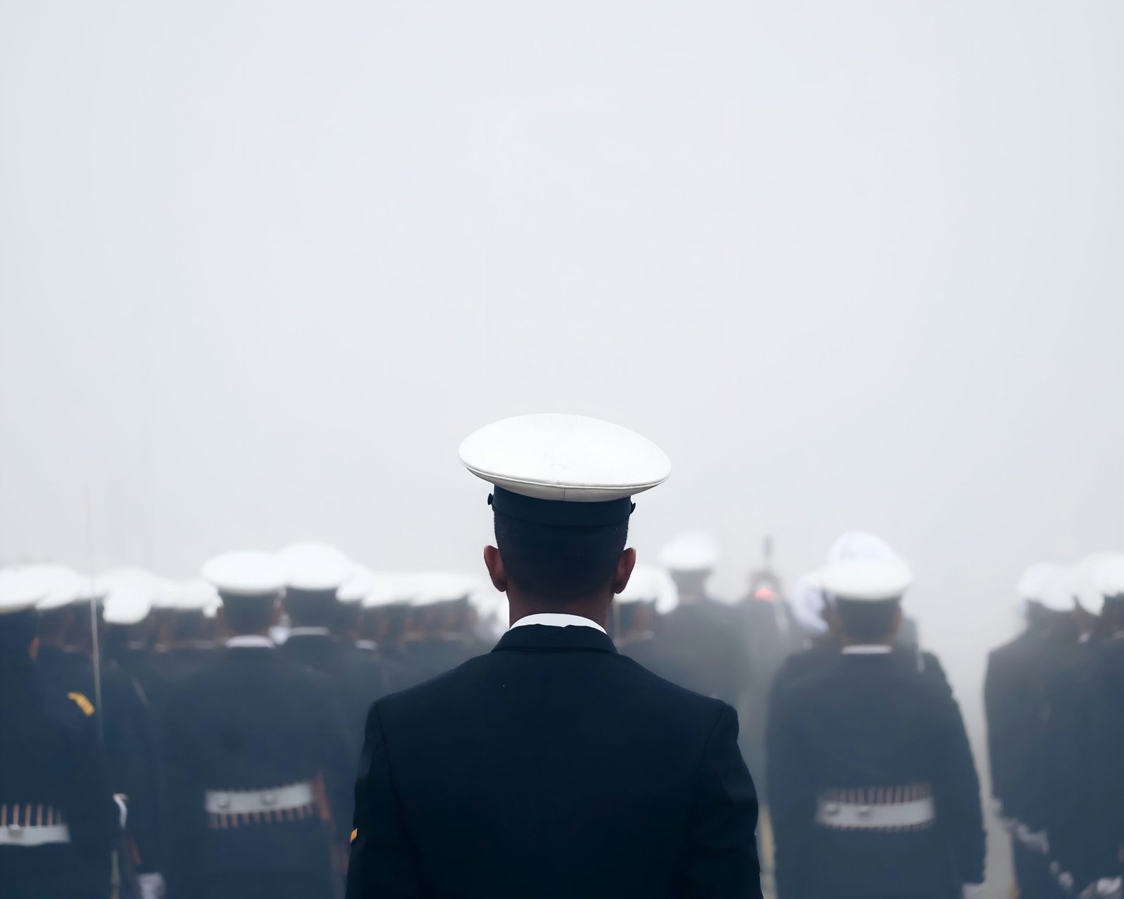 A navy officer stands before his troops in the fog.