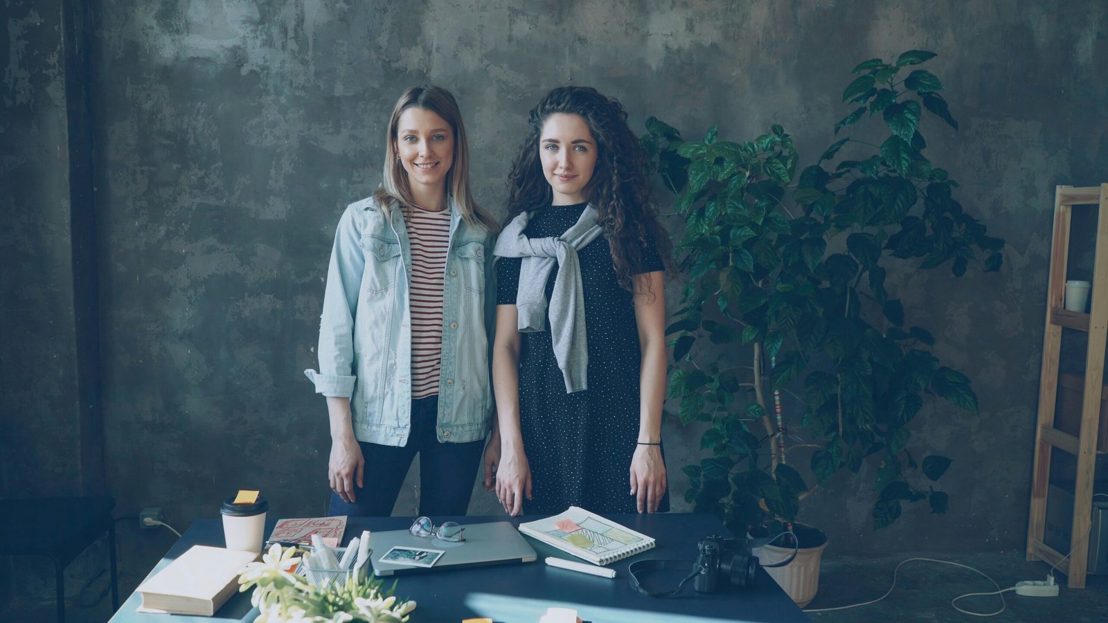 Two women stand behind a table in an office.