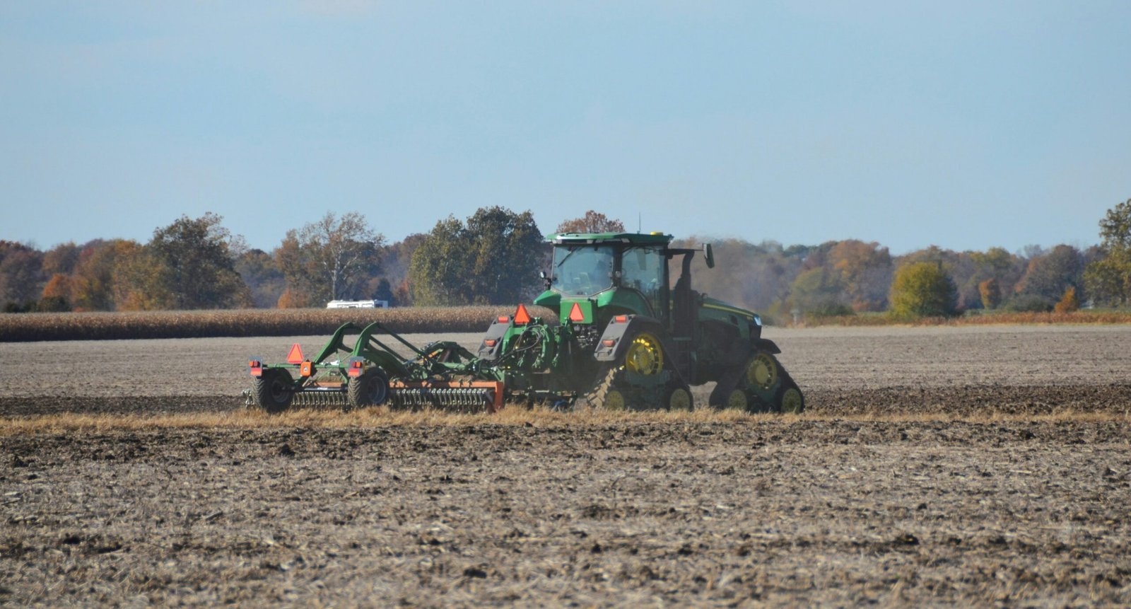 Green tractor plowing a field under a clear sky