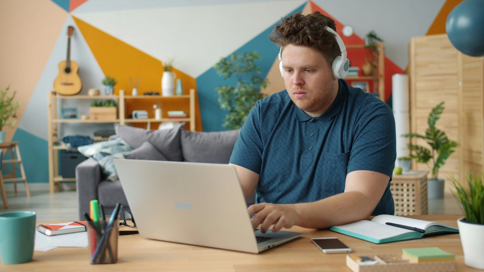 Man wearing headphones works on laptop at desk.