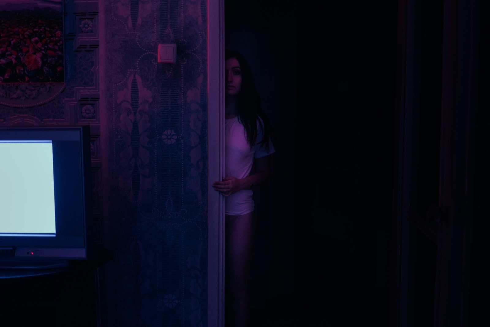 a woman standing in a dark room looking at a television