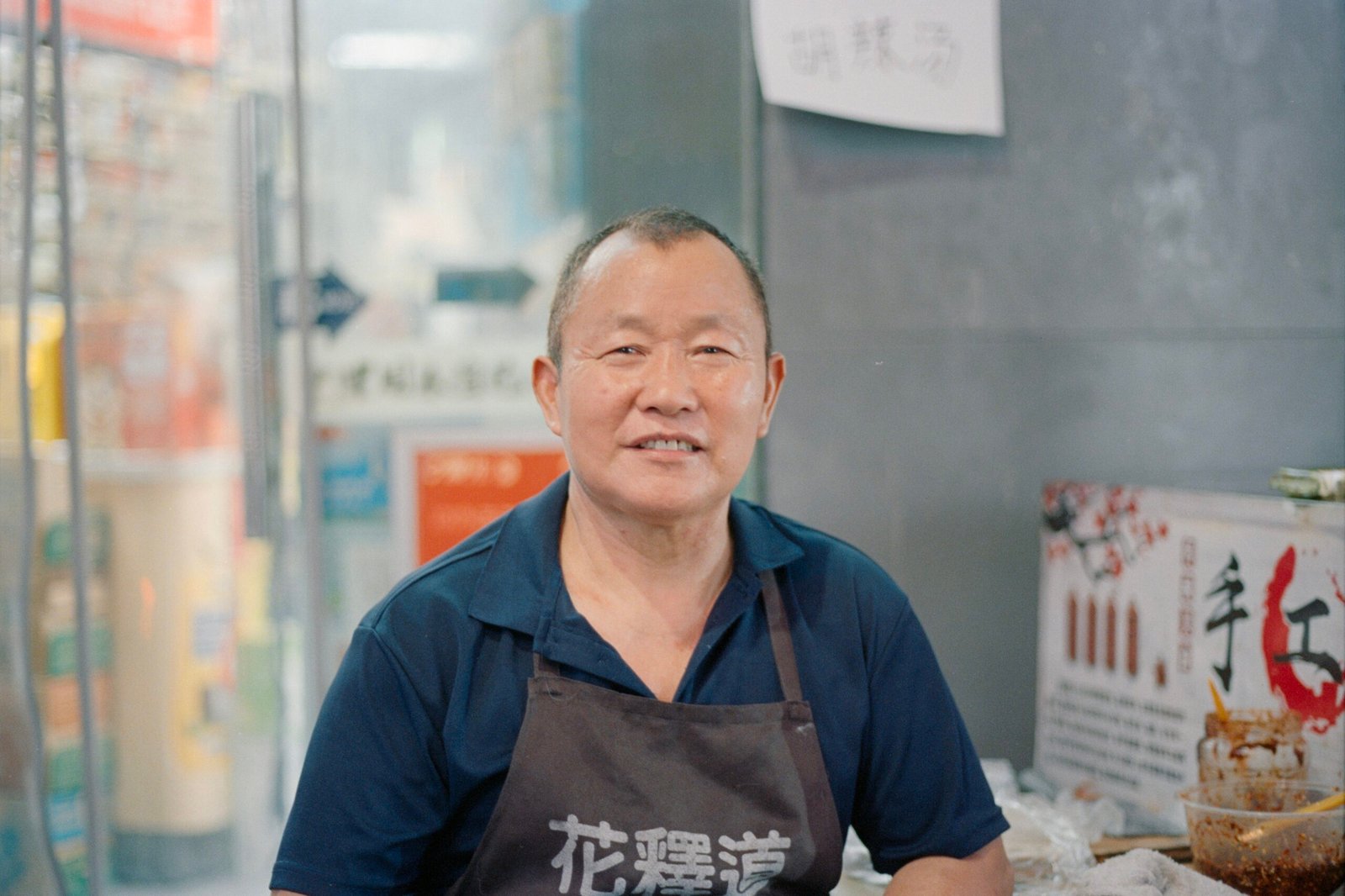 An elderly asian man wearing an apron smiles.