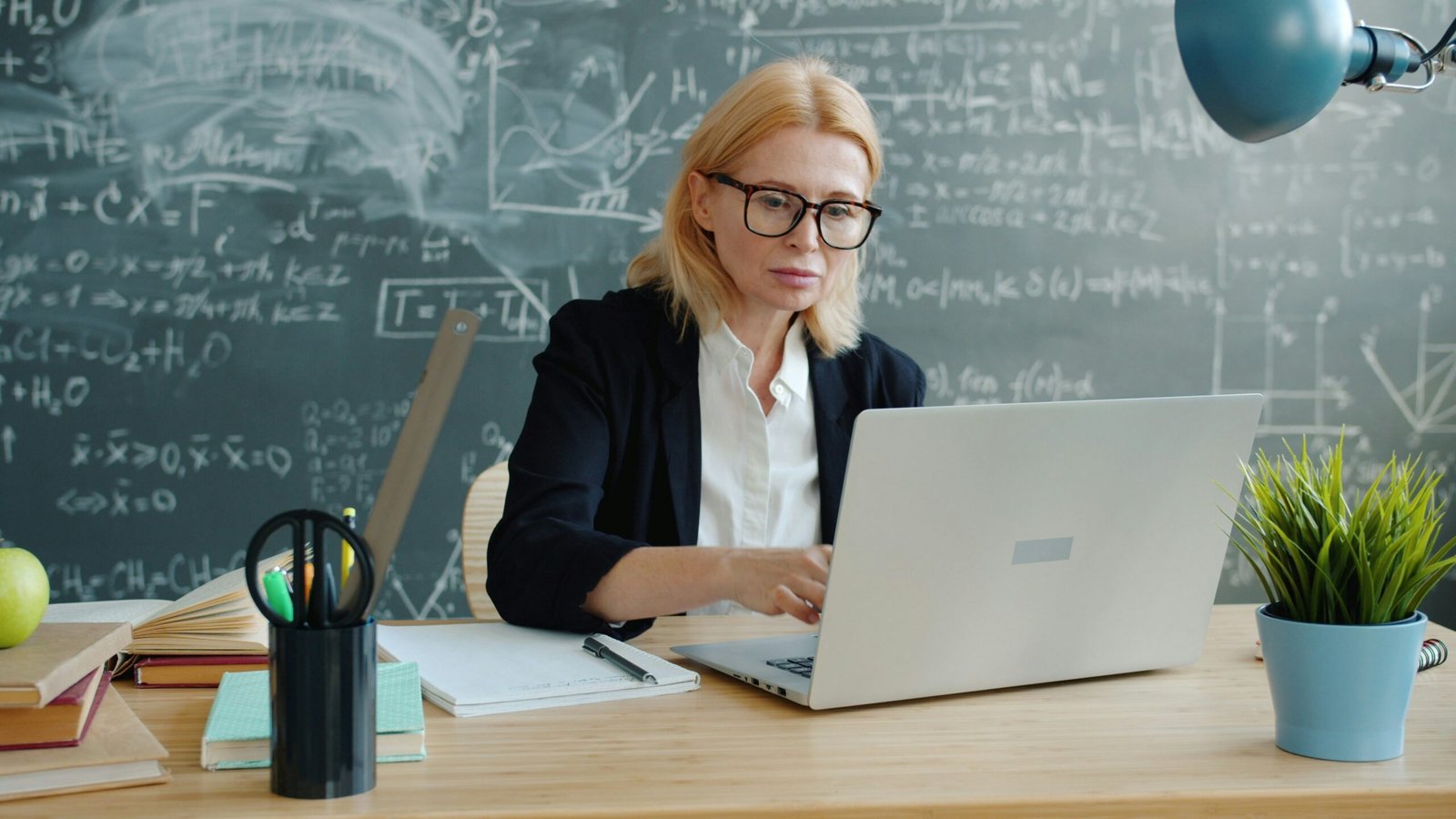 Woman working on a laptop in front of a chalkboard.