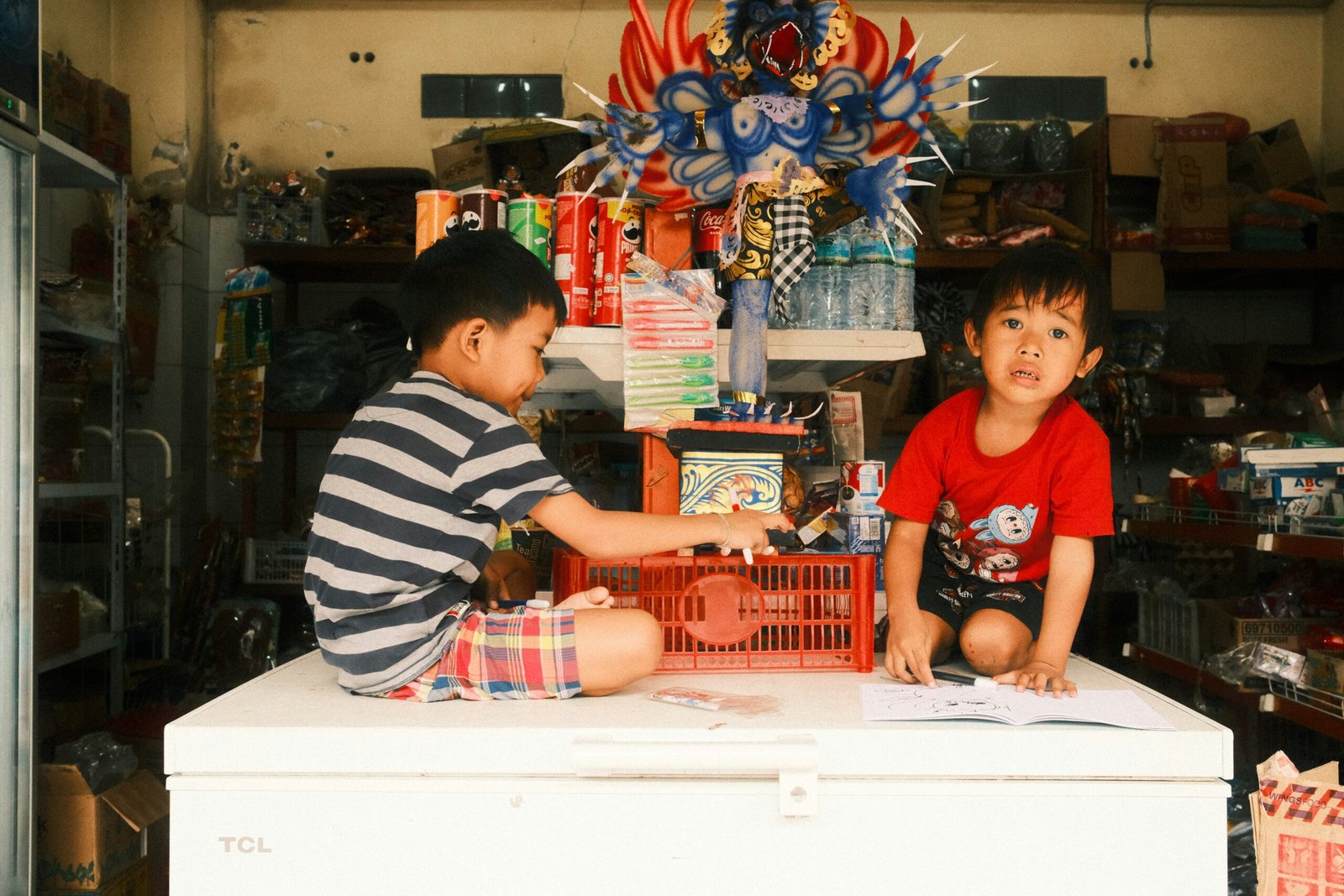 Two kids play on a freezer in a shop.