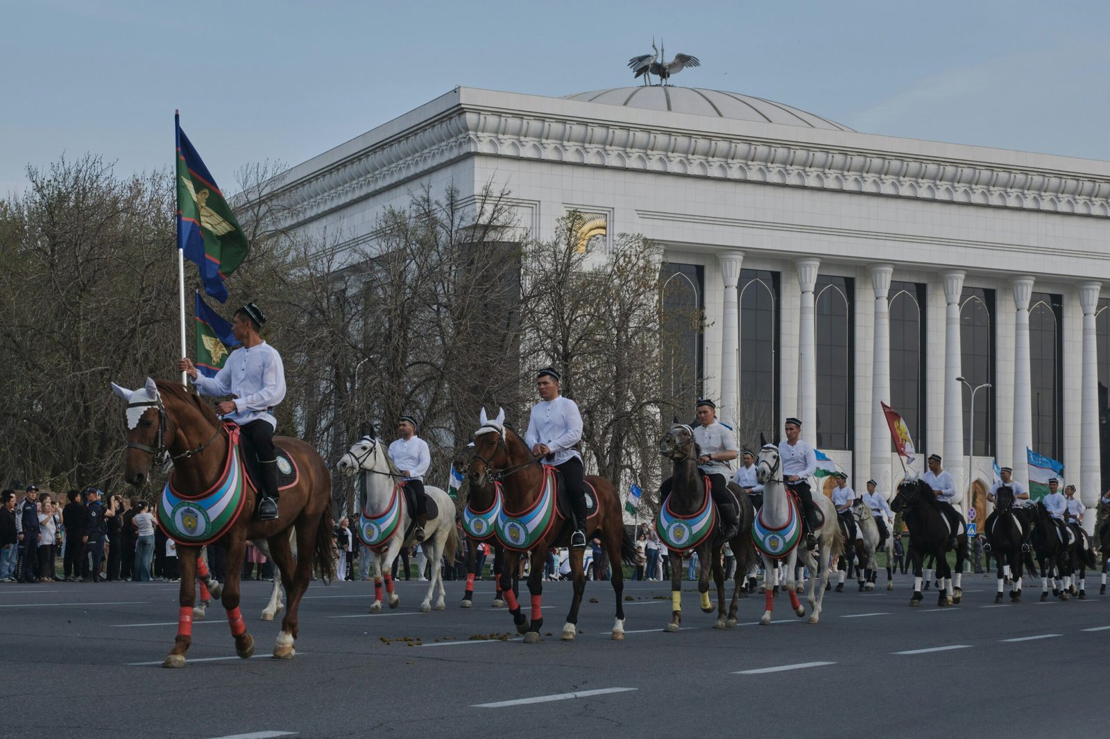 Horses and riders parade past a grand building.