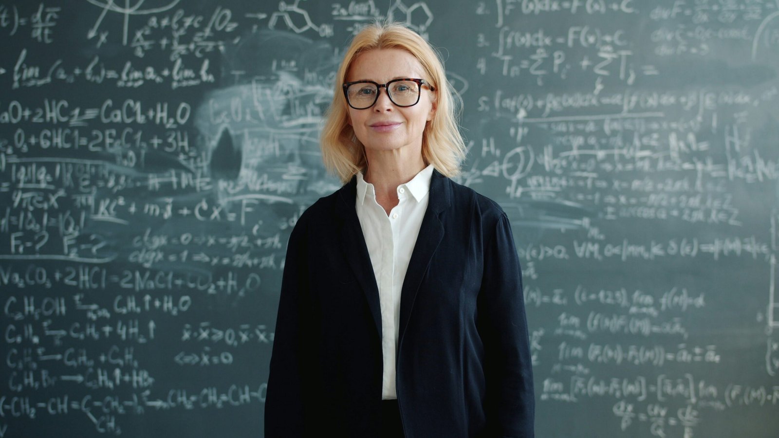 A woman stands in front of a chalkboard with equations.