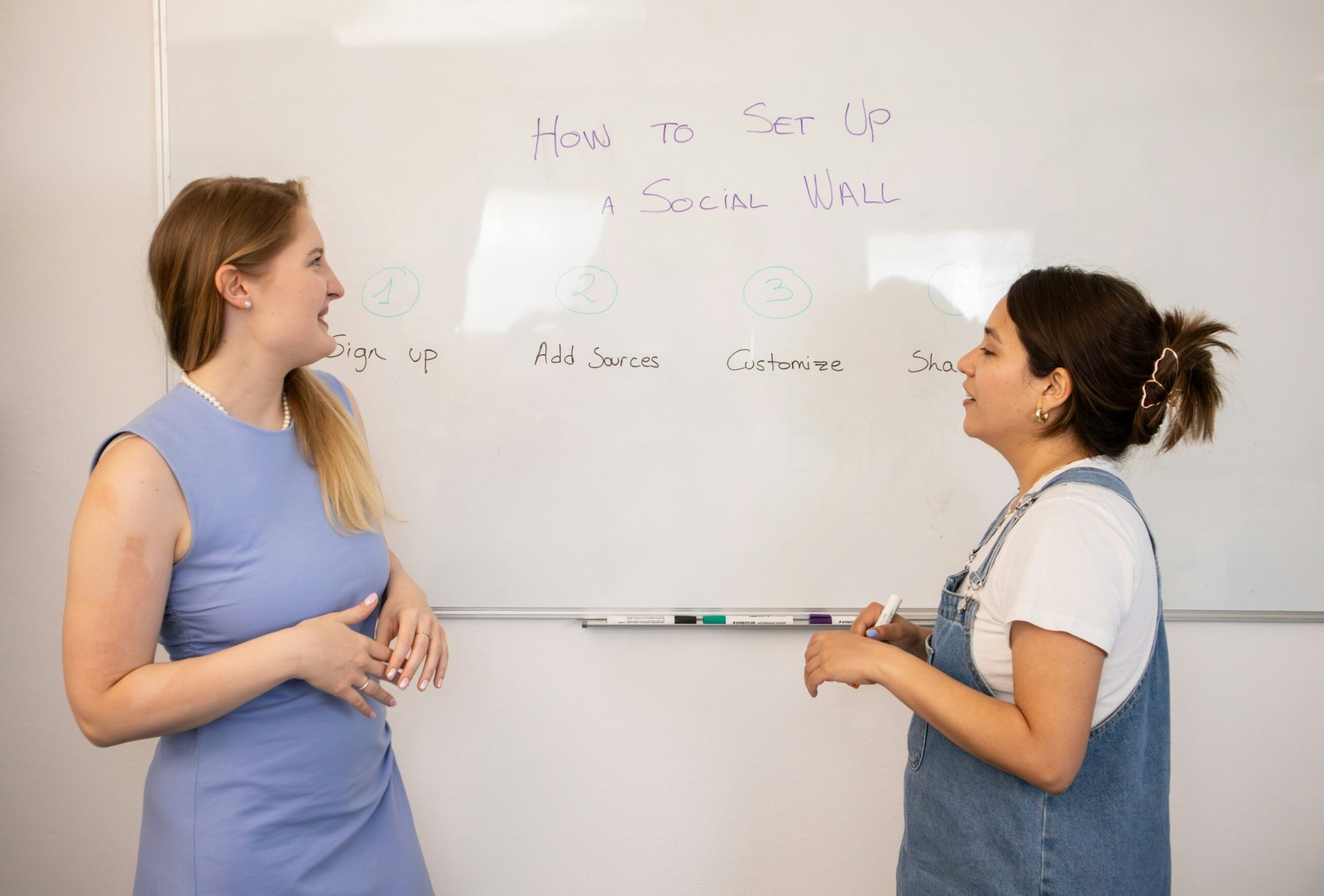 two women standing in front of a white board