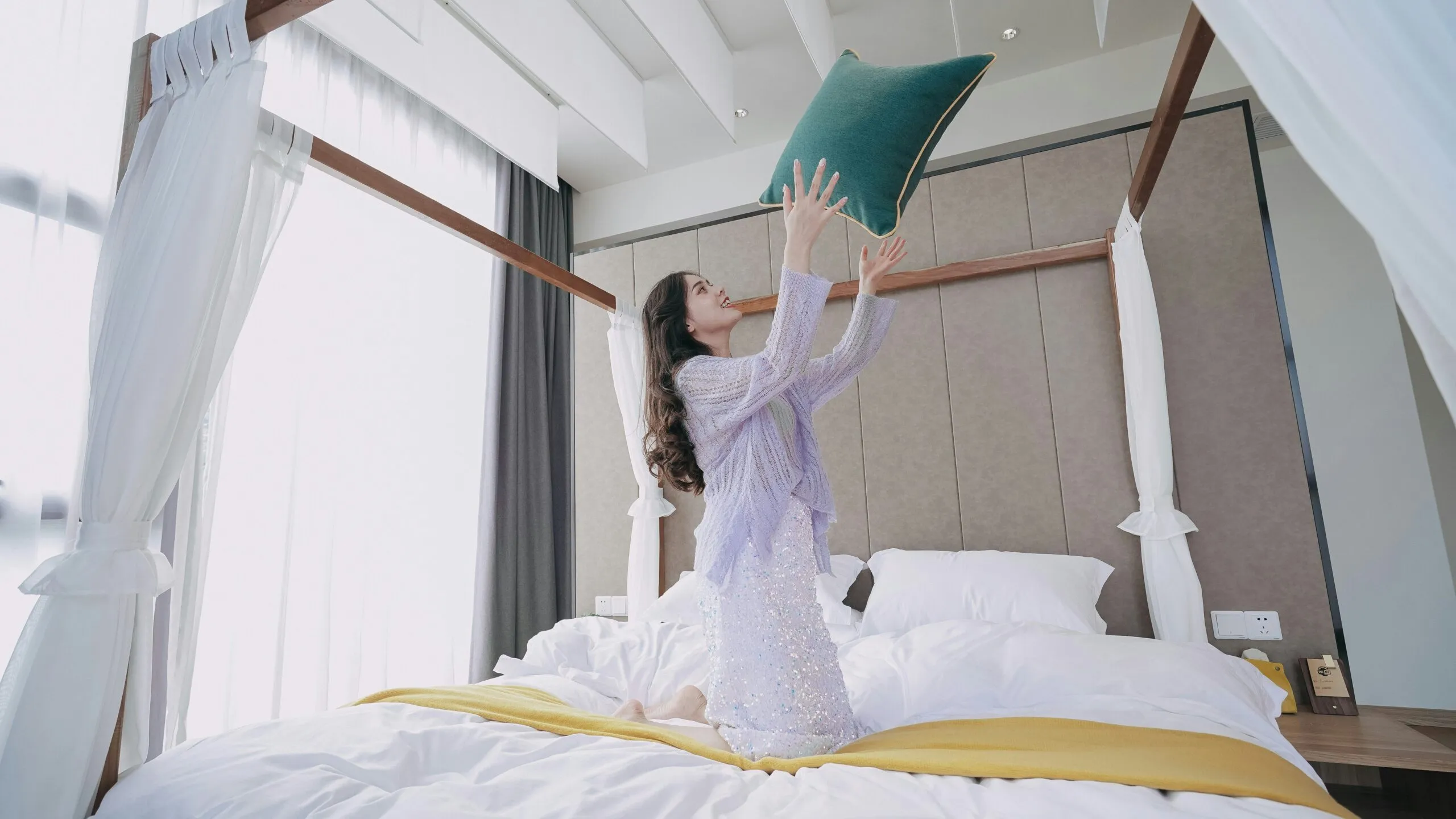 a woman in a white dress reaching up to a green pillow on a bed