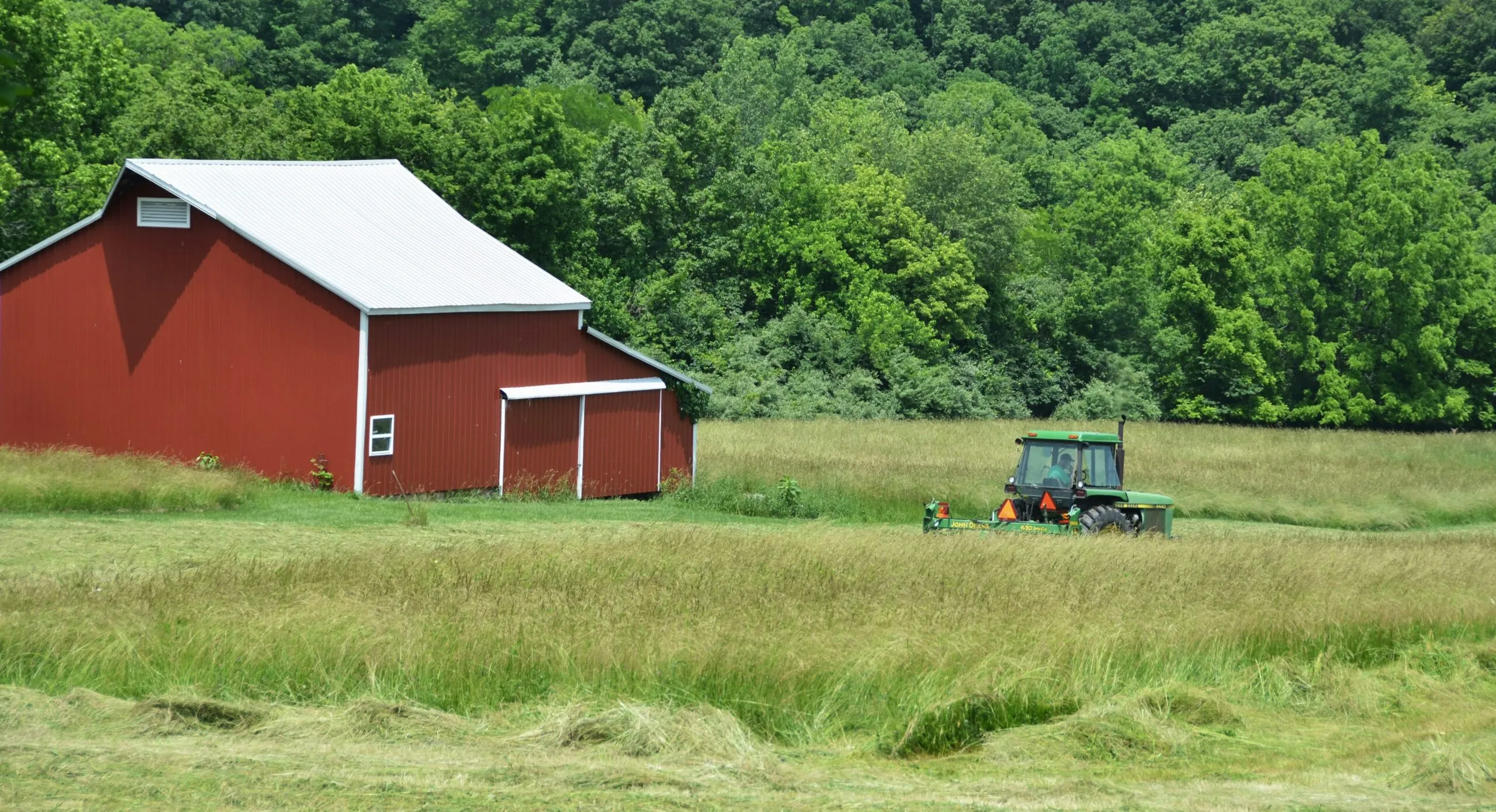 Red barn and tractor in a green field.