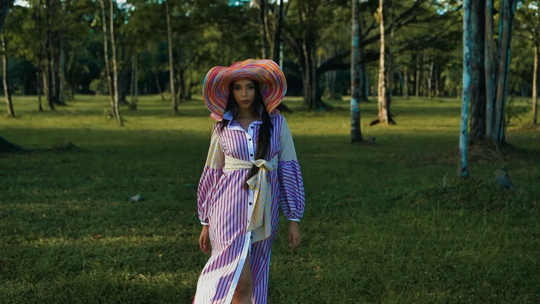 a woman in a dress and hat walking through the woods