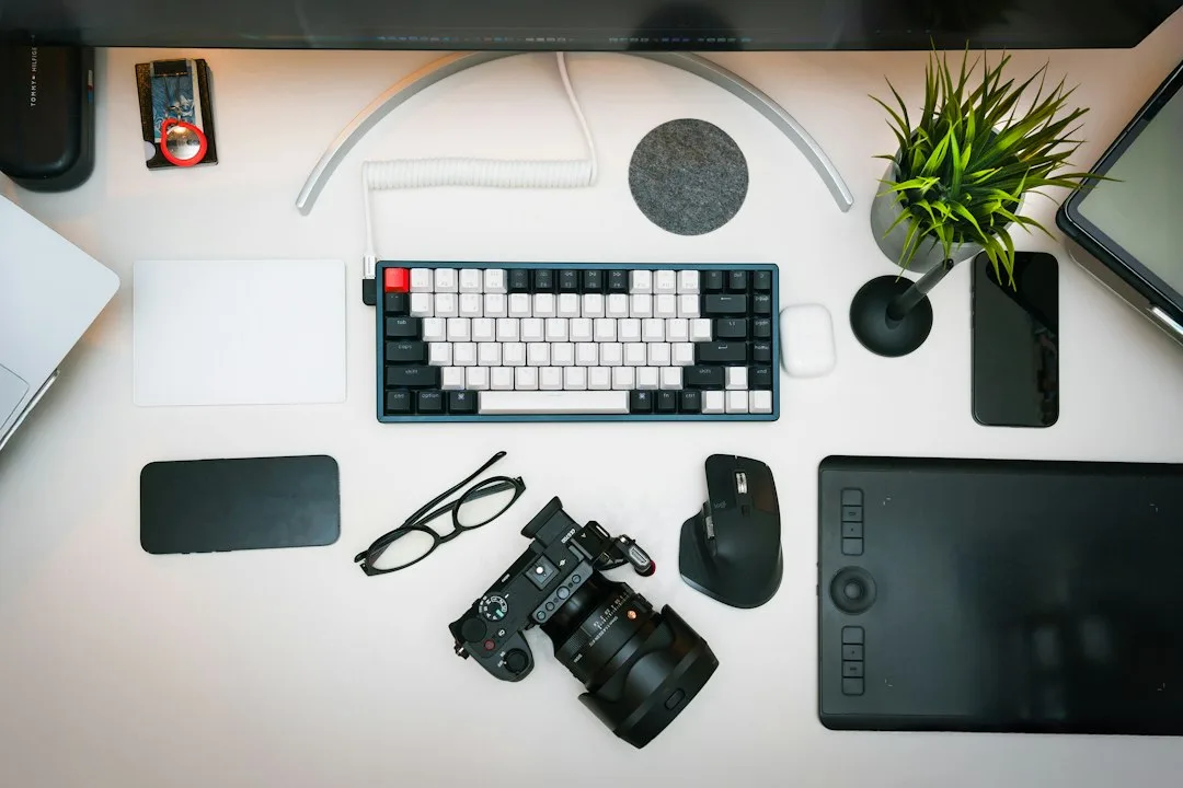 A desk with a keyboard, camera, mouse and other items