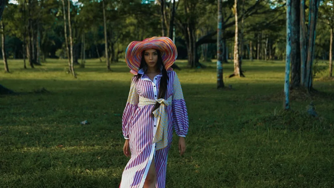 a woman in a dress and hat walking through the woods