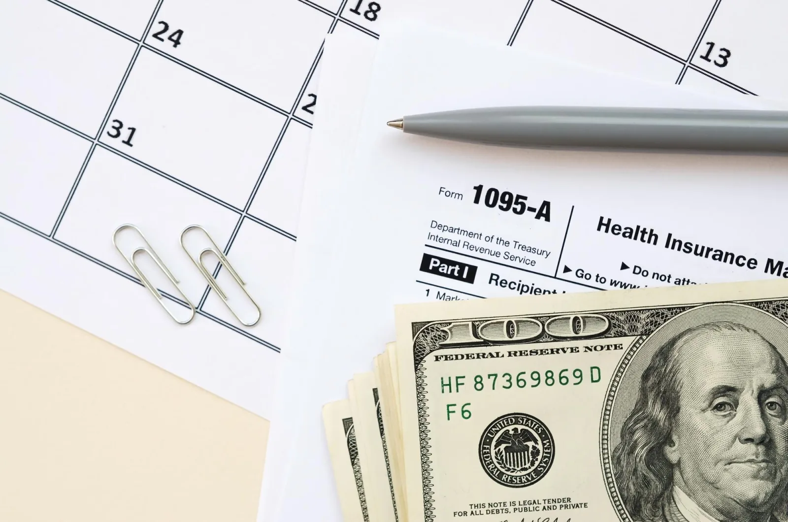 IRS Form 1095A Health Insurance Marketplace Statement tax blank lies with pen and many hundred dollar bills on calendar page