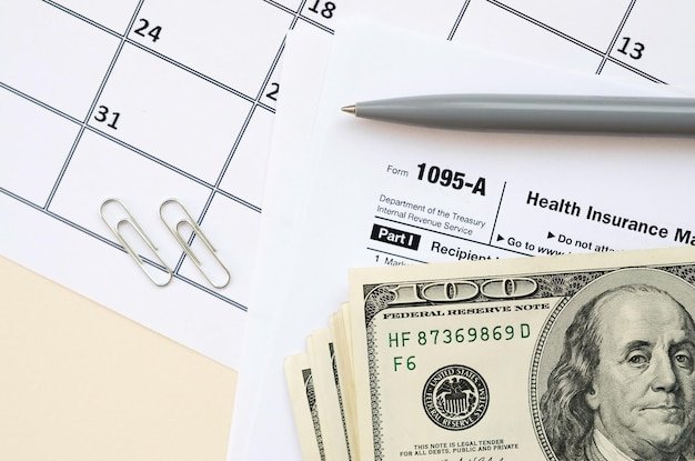 IRS Form 1095A Health Insurance Marketplace Statement tax blank lies with pen and many hundred dollar bills on calendar page