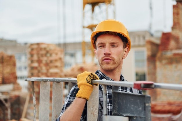 Ladder in hands Construction worker in uniform and safety equipment have job on building