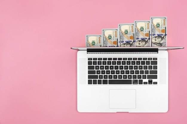 Laptop and dollar bills on color background flat lay