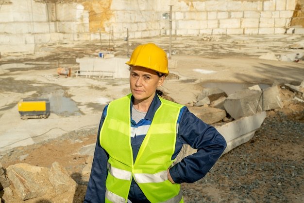 Mature female builder in workwear looking at you on constuction site