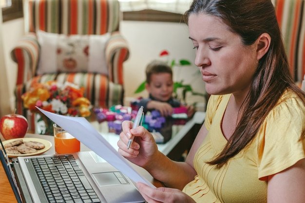 Mother working on the laptop in the living room while her son plays