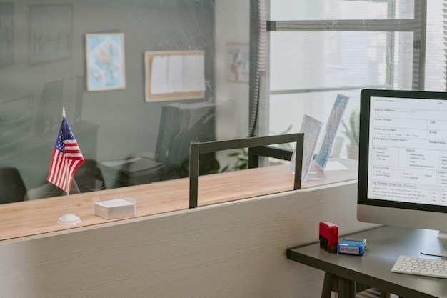 Office desk featuring computer screen and american flag displayed prominently beside it in workplace
