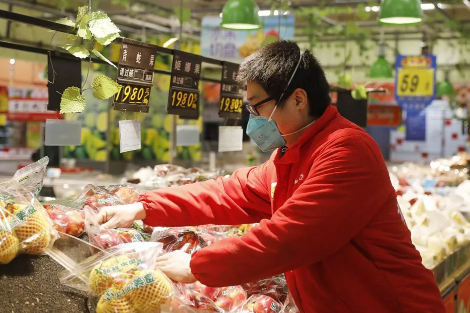 An Asian man in a mask arranging fruits in a Wuhan grocery store. Urban scene with focus on interaction.