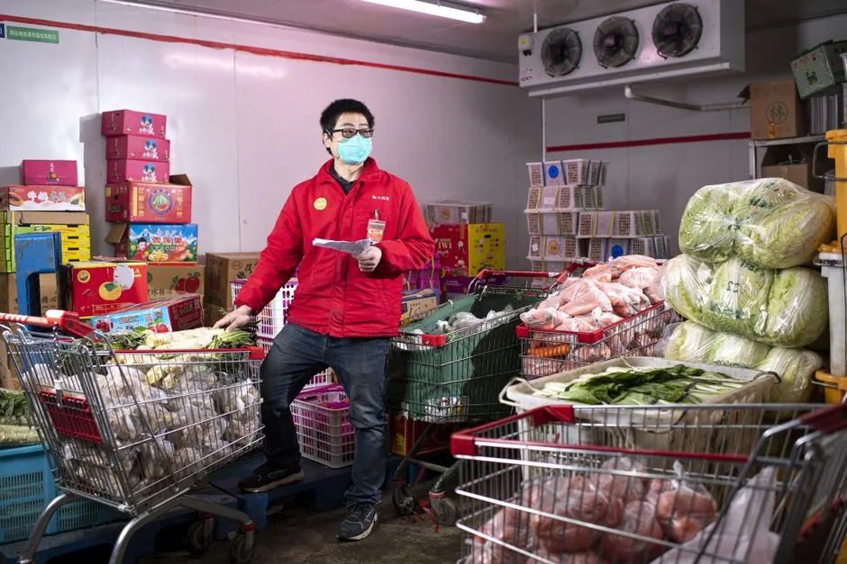 Asian man wearing red jacket and mask working in a store with shopping carts in Wuhan, China.